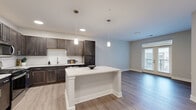 Located at 1420 W Deihl Rd in Naperville, IL, this well-appointed one-bedroom, one-bathroom unit offers a thoughtfully designed open-concept layout. The combined kitchen and living area serves as the heart of the home, showcasing rich dark cabinetry, white subway tile backsplash, light stone countertops, and a central kitchen island with pendant lighting overhead. Stainless steel appliances complete the kitchen, while light-toned hardwood-style flooring extends throughout the main living areas, creating a bright and cohesive aesthetic. The living room benefits from natural light and provides access to a private balcony through elegant French doors, offering views of the surrounding community. The spacious primary bedroom features plush carpeting, a ceiling fan, and a window that invites additional natural light. A dedicated walk-in closet with wire shelving systems provides generous storage. The bathroom is finished with a large glass-enclosed walk-in shower adorned with white subway tile, brushed nickel fixtures, and a dark vanity topped with a marble-style countertop. Neutral tones and clean lines throughout lend the space a modern, move-in-ready appeal.