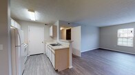 This single-floor unit on Claudia Drive in London, Ohio offers a practical and well-organized layout. The galley-style kitchen is equipped with white cabinetry, a double-basin stainless steel sink, a white refrigerator, and a range. A peninsula counter separates the kitchen from the adjoining living and dining areas, creating an open flow between spaces. Overhead fluorescent lighting illuminates the kitchen, while a pendant light fixture accents the dining area. Hard surface wood-look flooring runs throughout the main living areas, providing a clean and cohesive aesthetic.

The living area is accessed directly from the entry, which features a front door alongside a closet door, providing convenient storage upon arrival. The space is open and versatile, with neutral gray walls and natural light from a window facing the exterior.

The bedrooms are carpeted and finished with the same neutral gray tones. Each room features a walk-in or reach-in closet with wire shelving systems, offering functional storage. Textured ceilings are present throughout the unit.

The bathroom includes a single-sink vanity with wood-toned countertop, white cabinetry, a toilet, and a tub-shower combination, all finished with wood-look vinyl flooring for easy maintenance.