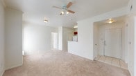 This single-story residence is designed with a practical, open layout that promotes a comfortable flow between living spaces. The main living area is generously proportioned, featuring neutral beige carpet, crown molding, and a ceiling fan with a light kit. It connects seamlessly to the kitchen via a peninsula-style breakfast bar, making the space feel open and cohesive. The entry transitions from tile flooring to carpet as it meets the living area.

The kitchen is well-equipped with warm oak cabinetry, light speckled countertops, a tiled backsplash, and white appliances including an electric range, microwave, and dishwasher. A stainless steel sink is positioned along the countertop, and tile flooring runs throughout the kitchen.

Two carpeted bedrooms offer natural light through large windows with views of surrounding greenery. The primary bedroom benefits from multiple windows on two walls, a ceiling fan, and access to a spacious walk-in closet outfitted with dual hanging rods and shelving.

Two bathrooms serve the unit. The primary bath features a soaking tub with tiled shower surround, oak cabinetry, and tile flooring. The secondary bath includes a single-sink vanity with a granite-style countertop, an oak cabinet, and a large mirror, all finished with matching tile flooring.