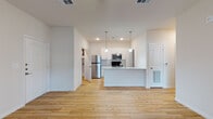 This well-designed single-floor unit offers a clean, contemporary aesthetic throughout, characterized by neutral tones, crisp white walls, and thoughtful finishes. The open-concept layout connects the living area to the kitchen, creating a spacious and functional flow. Light hardwood-style flooring runs throughout the main living spaces, enhancing the bright, airy atmosphere complemented by recessed lighting and natural light from exterior-facing windows and a glass-panel entry door.

The kitchen serves as a central focal point, featuring white shaker-style cabinetry, granite countertops, a subway tile backsplash, and a full suite of stainless steel appliances including a refrigerator, over-the-range microwave, and electric range. A peninsula with pendant lighting provides additional prep space and a casual dining option. A walk-in pantry with built-in shelving offers generous storage directly off the kitchen.

The bedroom is carpeted for comfort, fitted with a ceiling fan, and receives natural light through a window with blinds. The bathroom includes a wide vanity with granite countertops, white cabinetry, a wall-mounted mirror, and hardwood-style flooring that carries through from the main living areas. A soaking tub is also present. The overall space presents a move-in-ready, modern interior with consistent finishes throughout.