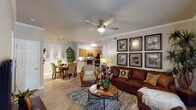 Located at 5799 Southland Dr in Mobile, Alabama, this single-floor residence offers a thoughtfully designed layout that balances comfort and functionality. The open-concept living and dining area serves as the heart of the home, featuring crown molding, wood-look flooring, and a ceiling fan overhead. The living room provides ample space for relaxed seating, accented by a gallery wall arrangement and large windows that invite natural light. Adjacent to the living area, the dining space features wainscoting detail and a dedicated nook framed by decorative wall art. The kitchen is outfitted with warm wood cabinetry, granite-style countertops, stainless steel appliances including a range, microwave, and dishwasher, and a breakfast bar for casual dining. A built-in desk area with a granite countertop offers a convenient workspace. The bedrooms are carpeted and generously sized, each featuring ceiling fans and walk-in closet access. The bathroom includes a single-sink vanity with wood cabinetry, a large mirror with overhead lighting, and a full tub-shower combination with tile surround. Throughout the residence, a cohesive neutral palette and consistent wood-look flooring tie the spaces together, creating a warm and inviting atmosphere.