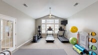 Located at 890 Quail Creek Blvd in Stow, Ohio, this dedicated fitness room offers a comprehensive workout environment within a single, efficiently designed space. The room's most striking architectural feature is its vaulted ceiling, which lends a sense of openness and airiness, complemented by a ceiling fan that ensures comfortable ventilation during workouts. A large, multi-pane window along one wall floods the space with natural light and provides pleasant outdoor views of the surrounding neighborhood.

The exercise room is outfitted with a well-rounded selection of equipment to support a variety of fitness routines. Cardio options include multiple treadmills and an elliptical machine, all positioned to face the windows. A wall-mounted flat-screen television provides entertainment during workouts. For strength training, the room features a adjustable weight bench, a full dumbbell rack with a range of weights, and a medicine ball rack. Stability and flexibility training is supported by an assortment of exercise balls and a dedicated fitness trainer unit. Rubber floor mats are placed beneath equipment for protection and safety.

A large wall mirror enhances the sense of space while allowing users to monitor their form. The room is accessed through a glass-paned interior door and is finished with neutral-toned carpet and soft gray walls, creating a clean, motivating atmosphere.