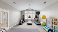 Located at 890 Quail Creek Blvd in Stow, Ohio, this dedicated fitness room offers a comprehensive workout environment within a single, efficiently designed space. The room's most striking architectural feature is its vaulted ceiling, which lends a sense of openness and airiness, complemented by a ceiling fan that ensures comfortable ventilation during workouts. A large, multi-pane window along one wall floods the space with natural light and provides pleasant outdoor views of the surrounding neighborhood.

The exercise room is outfitted with a well-rounded selection of equipment to support a variety of fitness routines. Cardio options include multiple treadmills and an elliptical machine, all positioned to face the windows. A wall-mounted flat-screen television provides entertainment during workouts. For strength training, the room features a adjustable weight bench, a full dumbbell rack with a range of weights, and a medicine ball rack. Stability and flexibility training is supported by an assortment of exercise balls and a dedicated fitness trainer unit. Rubber floor mats are placed beneath equipment for protection and safety.

A large wall mirror enhances the sense of space while allowing users to monitor their form. The room is accessed through a glass-paned interior door and is finished with neutral-toned carpet and soft gray walls, creating a clean, motivating atmosphere.