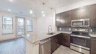 Located at 950 Town Lake Dr in College Station, Texas, this single-floor residence offers a well-designed layout with modern finishes throughout. The kitchen is a standout feature, showcasing rich dark-espresso cabinetry, granite countertops, and a peninsula island with pendant lighting overhead. A full suite of stainless steel appliances — including a refrigerator, electric range, microwave, and dishwasher — is complemented by a grey subway tile backsplash, adding a contemporary touch. Light wood-look flooring runs through the main living and kitchen areas, creating a warm yet modern aesthetic. Natural light filters in through windows near the dining area, enhancing the open feel of the space. The bathroom continues the refined design language with matching dark cabinetry, granite countertops, a large vanity mirror, and a tiled tub-shower combination, all set against light wood-look flooring and clean white walls. The bedroom features plush carpeting, a ceiling fan, and generous windows that invite natural light. The overall ambiance is clean, contemporary, and well-appointed, making this a functional and attractive living space in the heart of College Station.