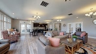 Located at 1000 Solomon Sq in Delaware, Ohio, this single-floor community clubhouse offers a thoughtfully designed gathering space that balances comfort with functionality. The open-concept main area features light hardwood flooring throughout, elegant chandelier lighting, and a striking stacked-stone accent wall anchored by a fireplace with a white mantel and wall-mounted television — serving as the visual centerpiece of the space. Large multi-pane windows along the perimeter flood the interior with natural light and provide views of the surrounding neighborhood.

The social hub transitions seamlessly into a fully equipped kitchen outfitted with dark espresso cabinetry, white countertops, stainless steel appliances, and a large island with bar seating — ideal for community events and gatherings. Adjacent to the kitchen, high-top bistro tables and chairs provide a casual dining area beneath warm chandelier lighting.

A cozy reading nook features plush seating and a gallery wall of framed historical photographs, adding a sense of local heritage to the space. A dedicated conference room with an oval table, upholstered seating, and a wall-mounted display screen provides a more private setting for meetings. French doors and exterior access points connect the interior to outdoor areas, enhancing the overall openness and flow of this inviting community facility.
