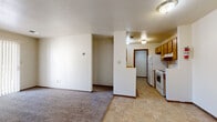This single-floor residential unit offers a straightforward, functional layout designed for comfortable everyday living. The open living area is finished with wall-to-wall carpet and neutral white walls, creating a clean, versatile canvas. A sliding glass door at one end of the living space allows natural light to flow in and provides a view of the outdoors, adding a sense of openness to the room.

The galley-style kitchen is efficiently arranged with warm honey-toned wood cabinetry lining both walls, providing generous storage. It is equipped with a white electric range and a refrigerator, along with a single-basin sink and tile-look flooring that contrasts with the carpeted living areas. A doorway at the end of the kitchen connects to additional areas of the unit.

The bedrooms continue the neutral aesthetic with plush carpeting and crisp white walls, offering quiet, comfortable spaces. The bathroom is finished with tile flooring that mirrors the kitchen, and features a full-size soaking tub with white tile surround, a toilet, and a towel bar. A textured ceiling treatment is consistent throughout the unit, giving the space a cohesive character. Overall, this unit presents a practical and livable layout with a warm, understated design.