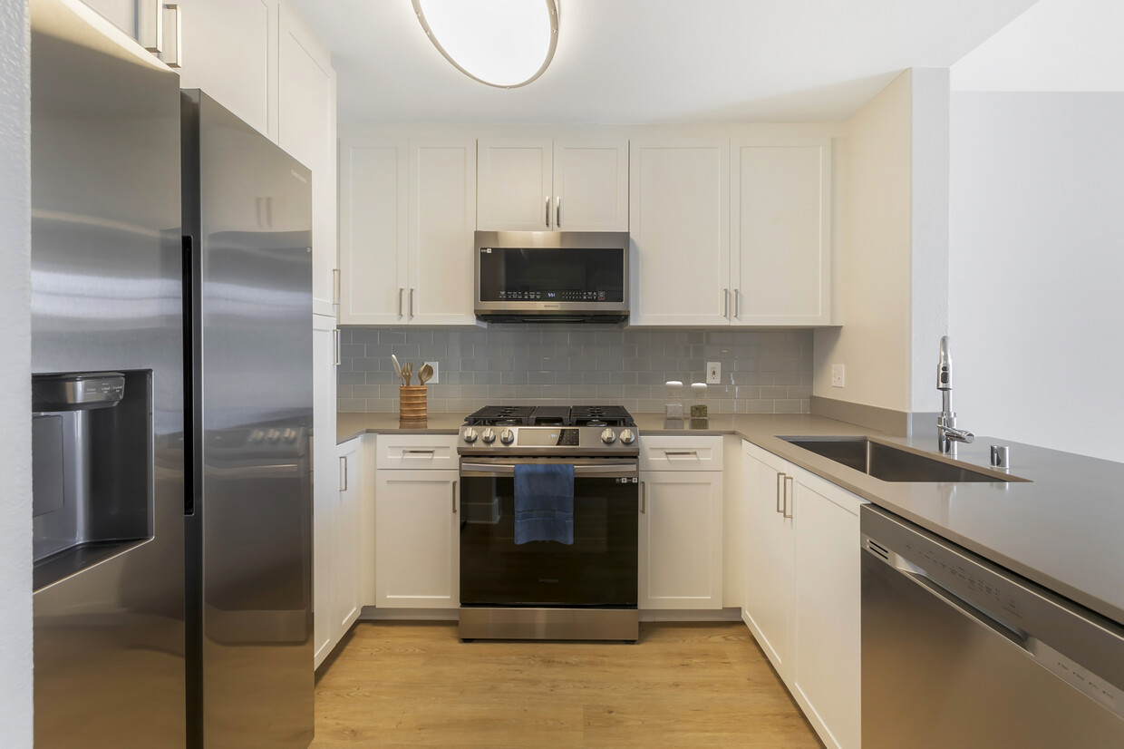 Renovated Package I kitchen with white cabinetry, grey quartz countertops, grey tile backsplash, stainless steel appliances, and hard surface flooring - Avalon Oak Creek