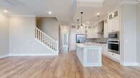 Located at 17014 Fairmount Way in Pineville, NC, this two-story home offers a thoughtfully designed layout spread across two floors. The main level features an open-concept living, dining, and kitchen area finished with warm hardwood-style flooring and neutral tones throughout. The chef's kitchen is a standout, showcasing floor-to-ceiling white shaker cabinetry with glass-front upper cabinets, a subway tile backsplash, stainless steel appliances including a gas cooktop, double wall oven, and French door refrigerator, all centered around a large white island with a built-in sink. Crown molding and recessed lighting add a polished touch, while a classic staircase with white balusters connects the two floors. Upstairs, the bedrooms are carpeted and bright, benefiting from large windows with neighborhood views. The generously sized primary bedroom includes access to a walk-in closet. The bathrooms are elegantly finished with large-format tile flooring, dual-sink white vanities, framed mirrors, a soaking tub, and a glass-enclosed shower. A dedicated laundry room with a full-size washer and dryer completes the upper level, adding everyday convenience to this well-equipped home.