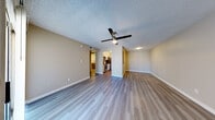 This single-floor residence offers a thoughtfully designed layout with a clean, modern aesthetic throughout. The open living area is finished with durable light-toned laminate wood flooring and neutral warm-beige walls, creating a bright and welcoming atmosphere. A ceiling fan with integrated lighting serves as both a functional and decorative element. A sliding glass door connects the living space to a private outdoor area, while a window allows natural light to filter in from outside.

The galley-style kitchen is efficiently designed with white shaker cabinetry, gray countertops, and a classic white subway tile backsplash. Stainless steel appliances — including an electric range, microwave, refrigerator, and dishwasher — complete the space, along with a stainless undermount sink fitted with a brushed nickel faucet.

The bedroom continues the laminate flooring found throughout the unit and features a ceiling fan, a window with outdoor views of surrounding greenery, and ample wall space for flexible furniture arrangement.

The bathroom showcases a floating wood-toned vanity with a white countertop, a large gold-framed mirror, and brushed nickel fixtures. A stacked washer and dryer unit is conveniently housed within the bathroom, adding practical in-unit laundry access. The textured ceilings are consistent throughout the space, complementing its overall understated, functional design.
