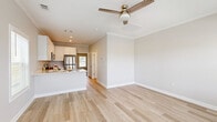 This thoughtfully designed single-story home offers a cohesive and functional layout across its one floor. The open-concept living and kitchen area is anchored by light-toned hardwood-style flooring that extends throughout the main living spaces, complemented by crisp crown molding and neutral warm-gray walls. Multiple windows with classic blinds flood the living room with natural light, while a ceiling fan with a brushed gold fixture adds both style and comfort. A front entry door with sidelights enhances the bright, welcoming atmosphere.

The kitchen is well-equipped with white shaker-style cabinetry, light countertops, and a full suite of stainless steel appliances including a refrigerator, range, built-in microwave, and dishwasher. A peninsula provides additional prep and serving space, seamlessly connecting the kitchen to the living area.

The spacious bedroom features plush carpeting, crown molding, a ceiling fan, and a window with outdoor views. It includes access to a dedicated closet with built-in hanging rods. The full bathroom is finished with a white vanity, framed mirror, and a shower-tub combo, maintaining the clean, consistent aesthetic found throughout the home.