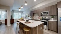 This thoughtfully designed one-bedroom, one-bathroom unit offers an efficient and modern layout across a single floor. The open-concept kitchen serves as a centerpiece, showcasing rich walnut-toned cabinetry, a stone-topped island with bar seating, and a full suite of stainless steel appliances including a range, microwave, dishwasher, and refrigerator. Stylish pendant lighting overhead enhances the contemporary aesthetic. The kitchen flows naturally into the living area, which benefits from a large window that invites natural light and provides outdoor views, creating an airy, comfortable atmosphere. Wood-style flooring runs throughout the main living spaces, adding warmth and visual continuity.

The bedroom is a cozy, well-proportioned retreat featuring windows on two walls that allow ample natural light. It connects directly to the full bathroom, which includes a glass-enclosed shower, a wood-toned vanity with a white countertop, and neutral tile flooring. Adjacent to the bathroom is a dedicated closet equipped with built-in shelving and hanging rods, providing organized storage. The unit's neutral color palette and clean architectural lines create a cohesive, modern ambiance throughout.