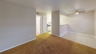 This single-story unit is thoughtfully laid out across a compact, functional floor plan. The living area serves as the heart of the space, featuring a combination of tile and carpet flooring, two windows fitted with blinds that allow natural light to filter in, and a front entry door flanked by additional windows, creating a bright and welcoming atmosphere. A ceiling fan is present in the adjoining areas, enhancing air circulation throughout.

The kitchen is positioned adjacent to the living area and is accessible via a pass-through counter, which also provides a casual dining or serving surface. The kitchen itself is equipped with white cabinetry, a gas range, a full-size refrigerator, and a sink, all set against light-colored countertops. A louvered closet door nearby adds practical storage access.

The bedrooms are carpeted and each features a ceiling fan with a light fixture and a window with blinds, providing both comfort and natural light. The rooms offer a quiet, functional environment suitable for a range of uses.

The bathroom is finished with light tile flooring and includes a pedestal sink, toilet, and a tub-shower combination with tiled surround, maintaining a clean and straightforward aesthetic throughout.