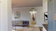 This thoughtfully designed two-bedroom, two-bathroom residence in Aliso Viejo, California offers a comfortable single-floor layout with a warm, neutral palette throughout. The living room serves as the heart of the home, featuring plush carpeting, crown molding, a ceiling fan with integrated lighting, and a window dressed with layered curtains that invite natural light. A hallway seamlessly connects the living area to the private bedrooms, lending the floor plan a logical and functional flow.

The galley-style kitchen is well-equipped with white cabinetry, dark countertops, stainless steel appliances including a range, microwave, and refrigerator, and wood-look flooring that adds warmth and durability. Adjacent to the kitchen, the dining area provides an intimate setting with its own distinct character.

The primary bedroom is generously proportioned, offering soft carpeting, a ceiling fan, and a window with natural views, accompanied by a dedicated walk-in closet featuring wire shelving for ample storage. The second bedroom mirrors this comfortable aesthetic. Both bathrooms are finished with white cabinetry, dark countertops, large mirrors, and wood-look tile flooring, each including a full tub-shower combination.