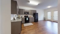 This single-floor unit offers a practical and efficiently designed layout across one bedroom and one bathroom. The kitchen serves as a central feature, outfitted with gray cabinetry extending to the upper walls for ample storage, granite-style countertops, and a full suite of black appliances including a refrigerator, range, microwave, and dishwasher. A single-basin sink with a window nearby adds convenience to the space. The kitchen flows directly into the living area, which is finished with warm wood-style flooring that runs throughout, creating a cohesive and open feel.

The bedroom is carpeted for comfort and features a window that allows natural light to fill the room, contributing to a bright and airy atmosphere. A ceiling fan provides additional ventilation.

The bathroom is clean and straightforward, featuring tile flooring, a full tub-shower combination with a curved curtain rod, a toilet, and a vanity with granite-style countertops and dark cabinetry below. White walls throughout the unit maintain a neutral, versatile backdrop suitable for a variety of furnishing styles.