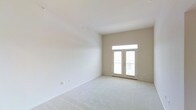 This single-floor space presents a clean, well-lit interior defined by a neutral palette and an open, airy atmosphere. The main room is immediately notable for its elevated ceilings, which enhance the sense of volume and openness throughout the space. Soft, light-toned wall-to-wall carpeting lines the floor, adding warmth and comfort underfoot while complementing the crisp white walls.

A standout architectural feature is the set of French doors positioned at the far end of the room, framed by a transom window above. This combination allows an abundance of natural light to pour in, brightening the interior and creating a seamless visual connection to the outdoors. The doors suggest access to a balcony or exterior area, further extending the livable feel of the space.

The walls are finished in a clean, neutral beige-white tone that reflects light effectively and provides a versatile backdrop. The overall design is simple and understated, emphasizing functionality and adaptability. The space is presented in a vacant state, offering a clear view of its architectural characteristics without the visual interruption of furnishings. The high ceilings, plentiful natural light, and well-proportioned layout make this a bright and inviting environment with strong potential for a variety of uses.