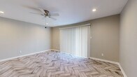 Located at 5200 SW 20th Terr in Topeka, Kansas, this 2-bedroom, 1-bathroom single-floor home offers a clean, modern aesthetic unified by striking herringbone-patterned wood-look flooring that runs throughout every room. The living room is a comfortable, open space featuring a ceiling fan with recessed lighting and a large vertical-blind-covered sliding door that allows natural light to filter in, creating a bright and airy atmosphere. The kitchen is well-appointed with grey shaker-style cabinetry, white countertops, a classic subway tile backsplash, and a full suite of stainless steel appliances including a refrigerator, range, microwave, and dishwasher. The primary bedroom is generously sized, equipped with a ceiling fan, and features two closets, providing ample storage. The second bedroom is equally inviting, with a ceiling fan, a window with blinds for natural light, and continuity in the herringbone flooring. The full bathroom includes a soaking tub with clean white subway tile surround and chrome fixtures. Neutral warm-grey tones on the walls throughout the home lend a cohesive, move-in-ready feel. The layout is efficient and well-connected, making excellent use of the available space.