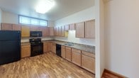 Located at 5400 Amber Valley Pkwy S in Fargo, North Dakota, this single-floor unit offers a practical and well-organized layout designed for comfortable everyday living. The kitchen is a standout feature, equipped with an abundance of light wood cabinetry extending to the upper walls, laminate stone-style countertops, a double-basin sink, and black appliances including a range, microwave, and dishwasher. Warm hardwood-style flooring runs throughout the kitchen, creating a clean and inviting workspace. The living area transitions to plush carpeting and is illuminated by natural light through wood-trimmed windows fitted with horizontal blinds. Baseboard heating units run along the walls, providing efficient warmth throughout the colder months. The bathroom features tile flooring in warm earth tones, a wood-cabinet vanity with a single sink, a wall mirror, and a full bathtub-shower combination. A dedicated in-unit laundry room includes a full-size washer and dryer set, tile flooring matching the bathroom, and overhead storage shelving, adding notable convenience. Throughout the unit, neutral wall tones and consistent trim details create a cohesive, understated aesthetic well-suited for a variety of living arrangements.