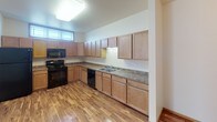 Located at 5400 Amber Valley Pkwy S in Fargo, North Dakota, this single-floor unit offers a practical and well-organized layout designed for comfortable everyday living. The kitchen is a standout feature, equipped with an abundance of light wood cabinetry extending to the upper walls, laminate stone-style countertops, a double-basin sink, and black appliances including a range, microwave, and dishwasher. Warm hardwood-style flooring runs throughout the kitchen, creating a clean and inviting workspace. The living area transitions to plush carpeting and is illuminated by natural light through wood-trimmed windows fitted with horizontal blinds. Baseboard heating units run along the walls, providing efficient warmth throughout the colder months. The bathroom features tile flooring in warm earth tones, a wood-cabinet vanity with a single sink, a wall mirror, and a full bathtub-shower combination. A dedicated in-unit laundry room includes a full-size washer and dryer set, tile flooring matching the bathroom, and overhead storage shelving, adding notable convenience. Throughout the unit, neutral wall tones and consistent trim details create a cohesive, understated aesthetic well-suited for a variety of living arrangements.