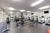 Located at 5130 E Ponce de Leon Ave in Tucker, GA, this fitness center offers a well-organized, single-floor exercise space designed to support a full range of workout routines. The room is thoughtfully laid out to maximize usability, featuring durable rubber flooring throughout that provides both safety and comfort during exercise.

The cardio section lines the windowed wall and includes multiple treadmills and elliptical trainers, all positioned to take advantage of the natural light and outdoor views provided by large floor-to-ceiling windows and glass-paned doors. Mounted flat-screen TVs are positioned above the cardio equipment for entertainment during workouts.

The strength training area is equally well-appointed, housing a multi-station cable machine, free weight benches, and additional resistance equipment. Full-length mirrors run along one wall, enhancing the sense of openness and allowing users to monitor their form during exercises.

Supplementary fitness tools, including medicine balls, a balance ball, and a wall-mounted exercise mat, are neatly organized along the back wall. Overhead flush-panel lighting ensures the space remains bright throughout. The clean, white walls and crisp trim contribute to a bright, modern ambiance, making this fitness center a functional and inviting environment for exercise.