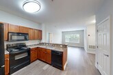 Located at 2 Windsor Woods Ln in Canton, Massachusetts, this two-bedroom, two-bathroom residence offers a well-designed single-floor layout with a thoughtful mix of functionality and comfort. The open-concept kitchen flows seamlessly into the living room, creating a connected and airy common area. The kitchen is equipped with warm-toned cabinetry, granite-style countertops, black appliances including a range, microwave, dishwasher, and refrigerator, and a peninsula that provides additional prep and dining space. Light wood-style flooring runs throughout the main living areas, adding a clean, modern feel.

The living room benefits from natural light through large windows overlooking greenery, lending a bright and welcoming ambiance. Both bedrooms are generously sized, with the primary bedroom featuring wide windows and plush carpeting, while the second bedroom offers hardwood-style flooring and ample natural light. Each bedroom is served by its own bathroom, both featuring tub-shower combinations, wood-toned vanities, and light, neutral finishes.

Additional highlights include an in-unit laundry room, three closets for abundant storage, a dedicated entrance, a hallway, and a utility room. The overall design is clean and contemporary, with a neutral color palette throughout.