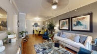 This thoughtfully designed single-floor residence offers a cohesive and stylish living experience across a well-organized layout. The open-concept living and dining area serves as the heart of the home, featuring warm hardwood flooring, crown molding, and a ceiling fan overhead. The living room is anchored by a tufted sofa set against a bold gray accent wall adorned with large framed artwork, while a glass coffee table and patterned area rug add layers of visual interest. The adjacent dining area accommodates a round glass table with upholstered chairs, complemented by a decorative mirror and gallery wall arrangement. The kitchen is well-equipped with rich cherry wood cabinetry, granite countertops, stainless steel appliances including a range and built-in microwave, and tile flooring — all opening toward the main living spaces for easy interaction. The primary bedroom features plush carpeting, a striking blue accent wall, a ceiling fan, and a window allowing natural light to filter in. It connects directly to a full bathroom with a tub-shower combination and a spacious walk-in closet with built-in shelving. A versatile secondary room serves as a dedicated home office with carpeted floors and an olive-toned accent wall. Completing the home is a conveniently located in-unit laundry area with side-by-side washer and dryer.