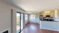 This single-floor residence offers a thoughtfully designed open-concept layout that seamlessly connects the living area and kitchen. Rich, dark hardwood flooring runs throughout the main living spaces, providing a warm and cohesive aesthetic. The living area is bright and airy, benefiting from abundant natural light that streams in through a large sliding glass door leading to a private balcony with outdoor views, as well as an additional window fitted with blinds. A ceiling fan overhead adds both comfort and a classic finishing touch to the space.

The kitchen is efficiently laid out with a peninsula-style counter featuring a dark stone countertop and an integrated double sink. White cabinetry provides ample storage, while stainless steel appliances — including a refrigerator, gas range, and built-in microwave — offer a modern, functional cooking environment. Flush-mount lighting illuminates the kitchen area effectively.

The bedroom is a quiet, comfortable retreat finished with soft wall-to-wall carpeting and neutral-toned walls, creating a calm and restful atmosphere. The bathroom is clean and functional, featuring a combination tub and shower unit with brushed nickel fixtures and coordinating towel bars. Throughout the residence, a consistent neutral color palette and clean finishes contribute to a move-in ready, understated modern appeal.
