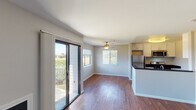 This single-floor residence offers a thoughtfully designed open-concept layout that seamlessly connects the living area and kitchen. Rich, dark hardwood flooring runs throughout the main living spaces, providing a warm and cohesive aesthetic. The living area is bright and airy, benefiting from abundant natural light that streams in through a large sliding glass door leading to a private balcony with outdoor views, as well as an additional window fitted with blinds. A ceiling fan overhead adds both comfort and a classic finishing touch to the space.

The kitchen is efficiently laid out with a peninsula-style counter featuring a dark stone countertop and an integrated double sink. White cabinetry provides ample storage, while stainless steel appliances — including a refrigerator, gas range, and built-in microwave — offer a modern, functional cooking environment. Flush-mount lighting illuminates the kitchen area effectively.

The bedroom is a quiet, comfortable retreat finished with soft wall-to-wall carpeting and neutral-toned walls, creating a calm and restful atmosphere. The bathroom is clean and functional, featuring a combination tub and shower unit with brushed nickel fixtures and coordinating towel bars. Throughout the residence, a consistent neutral color palette and clean finishes contribute to a move-in ready, understated modern appeal.
