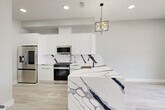 This thoughtfully designed two-bedroom, two-bathroom residence in Jersey City delivers a clean, modern aesthetic across its single-floor layout. Light-toned wide-plank hardwood flooring runs throughout, complementing a neutral white and gray palette that gives the space an open, airy feel.

The kitchen serves as a true centerpiece, showcasing a dramatic waterfall island clad in bold white-and-navy veined marble, matching backsplash, and sleek high-gloss white cabinetry. Stainless steel appliances — including a French door refrigerator, gas range, built-in microwave, and dishwasher — complete the space, which is illuminated by a striking geometric gold chandelier.

Both bathrooms continue the marble theme with floor-to-ceiling white marble-style wall tile, dark matte black hardware accents, gray slate-toned floor tile, and floating vanities with mirrored medicine cabinets — creating a spa-like atmosphere.

The two bedrooms are bright and clean, featuring recessed lighting and generous built-in closet storage. The primary bedroom includes a well-organized reach-in closet with built-in shelving and double hanging rods, while a secondary closet off the hallway provides additional storage. A connecting hallway ties the layout together efficiently, making the overall flow of the residence practical and intuitive.