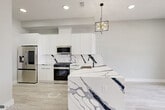 This thoughtfully designed two-bedroom, two-bathroom residence in Jersey City delivers a clean, modern aesthetic across its single-floor layout. Light-toned wide-plank hardwood flooring runs throughout, complementing a neutral white and gray palette that gives the space an open, airy feel.

The kitchen serves as a true centerpiece, showcasing a dramatic waterfall island clad in bold white-and-navy veined marble, matching backsplash, and sleek high-gloss white cabinetry. Stainless steel appliances — including a French door refrigerator, gas range, built-in microwave, and dishwasher — complete the space, which is illuminated by a striking geometric gold chandelier.

Both bathrooms continue the marble theme with floor-to-ceiling white marble-style wall tile, dark matte black hardware accents, gray slate-toned floor tile, and floating vanities with mirrored medicine cabinets — creating a spa-like atmosphere.

The two bedrooms are bright and clean, featuring recessed lighting and generous built-in closet storage. The primary bedroom includes a well-organized reach-in closet with built-in shelving and double hanging rods, while a secondary closet off the hallway provides additional storage. A connecting hallway ties the layout together efficiently, making the overall flow of the residence practical and intuitive.