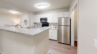 Located at 1200 Virginia Center Pkwy in Glen Allen, Virginia, this single-floor residence offers a thoughtfully designed layout with modern finishes throughout. The galley-style kitchen is a standout feature, showcasing crisp white cabinetry, granite countertops, stainless steel appliances including a refrigerator, range, microwave, and dishwasher, and wood-look flooring that extends into the common areas. A peninsula provides additional counter space and a natural transition toward the living area. The living room is bright and welcoming, featuring a ceiling fan, plush carpeting, and sliding glass doors that open to an outdoor space, allowing for generous natural light. The bedroom is generously sized with large windows framed by blinds that invite natural light, soft carpeting, and direct access to a well-appointed bathroom. The bathrooms feature granite-topped white vanities, wood-look flooring, and tub-shower combinations with clean white surrounds. A dedicated in-unit laundry area with a full-size washer and dryer adds everyday convenience. The overall aesthetic throughout the space is clean and contemporary, with a neutral color palette, consistent finishes, and functional details that create a comfortable and cohesive living environment.