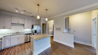 Located at 4531 Langdon Dr in Durham, NC, this well-designed one-bedroom, one-bathroom residence makes excellent use of its single-floor layout. The open-concept living area seamlessly connects the kitchen, dining, and living spaces, creating a cohesive and functional environment. The kitchen is a standout feature, boasting granite countertops, a central island with pendant lighting, gray shaker-style cabinetry, a full suite of stainless steel appliances including a French door refrigerator, dishwasher, range, and microwave, and rich hardwood-style flooring that extends throughout the main living areas. The living room is bright and airy, featuring crown molding, a ceiling fan, and French doors that invite natural light and provide outdoor access. The bedroom is a comfortable retreat with plush carpeting, a ceiling fan, a large window with outdoor views, and access to multiple closets. The full bathroom is elegantly appointed with a granite double-sink vanity, gray cabinetry, and a tub-shower combination. Additional practical features include an in-unit laundry area with a full-size washer and dryer, a pantry, and a utility room, rounding out this thoughtfully arranged and move-in-ready home.