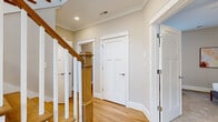 This two-story residence offers a thoughtfully designed layout across two floors, combining functional living spaces with refined architectural details. The main floor features an open-concept living, dining, and kitchen area bathed in natural light from large windows. The living room provides a welcoming atmosphere with warm hardwood floors and a bright bay window alcove. The kitchen is outfitted with white shaker cabinetry, granite countertops, stainless steel appliances, and a peninsula that flows seamlessly into the dining area, which features crown molding and additional window views. A dedicated laundry room with side-by-side washer and dryer adds everyday convenience on this level. The upper floor hosts three carpeted bedrooms, including a generously sized primary suite with a walk-in closet and private access to additional rooms. The primary bathroom features a dual-sink vanity with granite countertops, white cabinetry, marble-style tile flooring, and gold-accented lighting fixtures. Additional bathrooms are finished with marble-tile walk-in glass showers and granite vanities. A handsome wood staircase with white balusters connects both floors, anchoring the home's classic yet contemporary aesthetic throughout.