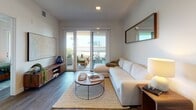 Located along E Seaside Way in Long Beach, California, this thoughtfully designed single-floor residence combines modern aesthetics with comfortable, functional living. The open layout is unified by warm hardwood-style flooring that flows seamlessly throughout.

The kitchen is a standout feature, outfitted with sleek, dark cabinetry, stainless steel appliances including a gas range and built-in microwave, a striking black tile backsplash, and clean white countertops. Open shelving adds both style and practicality to this well-appointed culinary space.

The living room is bright and welcoming, anchored by a sectional sofa and sliding glass doors that open directly onto a private balcony, allowing for an effortless indoor-outdoor connection with views of the surrounding neighborhood.

Multiple bedrooms offer distinct character: one features a modern sliding frosted glass barn door and ceiling fan, while another enjoys direct balcony access with generous natural light. A third bedroom includes a clerestory window that draws in daylight while maintaining privacy.

The bathroom is cleanly finished with a dark vanity, backlit mirror, and a full tub-shower combination framed by large-format tile. A hallway with louvered storage connects the spaces with practical elegance. Throughout, recessed lighting and a neutral palette create a calm, cohesive ambiance ideal for coastal living.