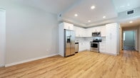 This well-designed single-floor unit offers a clean, modern aesthetic with warm wood-look flooring running consistently throughout every room, tying the space together cohesively. The kitchen is a standout feature, outfitted with crisp white shaker-style cabinetry, light countertops, and a full suite of stainless steel appliances including a French door refrigerator with ice and water dispenser, an electric range with over-the-range microwave, and a dishwasher. Recessed lighting illuminates the kitchen area, highlighting the ample cabinet storage above and below the counters. The open living and dining area is generously proportioned, featuring multiple windows dressed with white horizontal blinds that allow natural light to fill the space. Neutral, light gray walls complement the flooring and create a versatile backdrop throughout. The bedrooms are well-sized, each benefiting from natural light through sizable windows and ceiling fans for added comfort. The bathroom features a walk-in shower with white tile surround, a marble-style base, and polished chrome fixtures, maintaining the clean and contemporary look found throughout the unit. The overall ambiance is bright, fresh, and move-in ready.