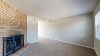 This two-story home offers a practical and comfortable layout spread across two levels, connected by an interior staircase. The main living area is a generously sized, carpet-floored space highlighted by a full-height brick fireplace surround — a standout architectural feature that adds warmth and character to the room. Neutral-toned walls and multiple windows allow natural light to filter in, creating a bright and open atmosphere. A front entry door is flanked by two windows that offer views of the surrounding greenery.

The kitchen is functional and well-appointed, featuring gray cabinetry, wood-look flooring, a full suite of white appliances including a refrigerator, electric range, microwave, and dishwasher, along with a ceiling fan nearby. A sliding glass door provides additional light and access to the exterior.

The bedrooms are carpeted and finished with neutral walls, each featuring windows that bring in natural light. The bathrooms are clean and practical, with one featuring a tub-shower combination, wood-look tile flooring, and gray vanity cabinetry with a white countertop. A second bathroom provides a vanity with a marble-look countertop and a mirrored medicine cabinet. The home also includes a dedicated in-unit laundry area with a full-size washer and dryer and overhead shelving.
