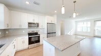 Located at 1700 Ranch Rd in Nokomis, Florida, this two-story home offers a well-organized layout spread across two levels. The ground floor houses an attached garage with an automatic opener and a staircase leading up to the main living areas, which occupy the upper floor.

The upper level is where the home truly opens up, featuring a combined dining room, kitchen, and living room that creates a cohesive, open-concept gathering space. Light wood-style flooring flows throughout the common areas and staircases, lending a clean, contemporary feel. The kitchen is complemented by a dedicated pantry fitted with wire shelving for generous storage. A separate laundry area and hallway round out the functional spaces on this floor.

The two bedrooms are carpeted and filled with natural light from large windows. The primary bedroom includes a ceiling fan and connects to a walk-in closet with wrap-around wire shelving. Additional closets throughout the home provide ample storage. The two bathrooms are finished with wood-look flooring, white subway tile tub-and-shower surrounds, and granite-topped vanities.

Outside, the property enjoys open, sunny surroundings with manicured lawn areas and expansive rural views — a hallmark of Nokomis's relaxed, spacious character.