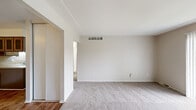 This single-floor residence in Clinton Township, Michigan, features a thoughtful layout comprising two bedrooms, one bathroom, a kitchen, and a connecting hallway. The living area is finished with neutral-toned carpet and painted in light, warm tones, creating a clean and understated ambiance. Overhead HVAC vents are integrated into the ceiling, ensuring consistent climate control throughout the space.

The generously sized primary bedroom features plush carpeting, a ceiling fan with light fixture, a window with vertical blinds that allows natural light and outdoor views, and a built-in closet with sliding panel doors and shelving for organized storage. The second bedroom is similarly carpeted and maintains the same neutral palette.

The kitchen stands out with warm wood-toned cabinetry featuring decorative glass inserts, a peninsula layout with a built-in sink, electric range, and refrigerator. Wood-look flooring grounds the kitchen and hallway, offering a practical contrast to the carpeted living spaces.

The bathroom is bright and clean, finished with white tile flooring and a tiled tub/shower surround, complemented by a vanity and a window with vertical blinds that introduces natural light. The overall design is functional and well-maintained, making this a comfortable and practical residence.