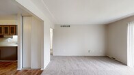 This single-floor residence in Clinton Township, Michigan, features a thoughtful layout comprising two bedrooms, one bathroom, a kitchen, and a connecting hallway. The living area is finished with neutral-toned carpet and painted in light, warm tones, creating a clean and understated ambiance. Overhead HVAC vents are integrated into the ceiling, ensuring consistent climate control throughout the space.

The generously sized primary bedroom features plush carpeting, a ceiling fan with light fixture, a window with vertical blinds that allows natural light and outdoor views, and a built-in closet with sliding panel doors and shelving for organized storage. The second bedroom is similarly carpeted and maintains the same neutral palette.

The kitchen stands out with warm wood-toned cabinetry featuring decorative glass inserts, a peninsula layout with a built-in sink, electric range, and refrigerator. Wood-look flooring grounds the kitchen and hallway, offering a practical contrast to the carpeted living spaces.

The bathroom is bright and clean, finished with white tile flooring and a tiled tub/shower surround, complemented by a vanity and a window with vertical blinds that introduces natural light. The overall design is functional and well-maintained, making this a comfortable and practical residence.