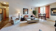 This single-floor residence offers a thoughtfully designed layout that balances comfort and functionality. The open living area is anchored by plush carpeting, a pendant light fixture, and large windows dressed in warm-toned curtains that invite generous natural light and outdoor views. A dining area adjacent to the living space provides a relaxed setting for everyday meals.

The primary bedroom features a soothing color palette with a bold accent wall, a ceiling fan, and windows offering leafy outdoor views, creating a calm and restful retreat. A second bedroom is versatile and well-lit, with carpeted floors, a baseboard heater, and a window overlooking the surroundings — ideal as a guest room, home office, or flex space.

The two bathrooms are finished with wood-look flooring, warm-toned cabinetry, and tub-shower combinations with curtain enclosures, offering a clean and practical design. One bathroom features bold yellow accent walls, while the other presents a lighter, neutral palette with a warm wood vanity.

A dedicated laundry area houses a full-size top-loading washer and dryer with built-in shelving above, adding everyday convenience. Throughout the residence, a cohesive design sensibility ties each space together with warm tones, natural textures, and functional details.