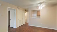 Located at 710 Lindh Rd in Gulfport, Mississippi, this single-floor residence offers a functional and comfortable layout designed for easy living. The living area features rich, dark hardwood-style flooring that extends throughout the space, complemented by neutral beige walls and a ceiling fan with a built-in light fixture that promotes airflow and ambient lighting. A pass-through opening connects the living area to the kitchen, which is equipped with light wood cabinetry and a white refrigerator, creating an open and communicative flow between the two spaces. The kitchen's pass-through counter adds a convenient bar-style ledge, enhancing the interactive nature of the layout. Multiple closet doors visible from the main living space suggest generous storage options throughout the unit. A hallway leads to a dedicated laundry area with in-unit washer and dryer hookups, adding a practical and desirable convenience. HVAC vents are well-positioned throughout the space, ensuring consistent climate control. The overall ambiance is clean, bright, and move-in ready, with a simple and cohesive design aesthetic that provides a welcoming environment suitable for a variety of living arrangements.