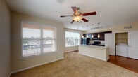 This two-bedroom, two-bathroom residence in Spring, Texas offers a thoughtfully designed single-floor layout that blends functionality with modern finishes. The entry hallway, finished with rich hardwood-style flooring, leads into a bright, open-concept living and kitchen area filled with natural light from multiple large windows dressed with blinds. A ceiling fan with a light fixture anchors the living space, which features warm, neutral-toned carpet.

The kitchen is a standout, showcasing dark espresso cabinetry, granite countertops, and a suite of black appliances including a refrigerator, range, and built-in microwave. A peninsula with a double sink and elegant pendant lighting serves as both a prep area and casual dining space, creating a natural divide between the kitchen and living room. A dedicated in-unit laundry area with a full-size washer and dryer is conveniently accessible from the kitchen.

Both bedrooms are carpeted and offer generous proportions with ample natural light. The primary bedroom connects to a private bathroom with dark cabinetry, a white vanity, hardwood-style flooring, and a walk-in closet. The second bathroom features a tub-shower combination with tiled surround and matching dark cabinetry, maintaining a consistent design aesthetic throughout the home.
