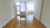 This single-floor space offers a clean, well-maintained interior that combines classic design elements with a bright, open atmosphere. The standout feature of the main living area is the beautifully polished parquet hardwood flooring, laid in a distinctive geometric pattern that adds warmth and character to the space. Large windows dressed with horizontal blinds line the walls, allowing an abundance of natural light to fill the room and create an airy, welcoming ambiance. A glass-paneled door provides an additional source of light and offers access to an adjacent area or exterior space. The smooth, neutral-toned walls serve as a versatile backdrop, lending a sense of openness throughout. The layout is thoughtfully open, allowing for flexible furniture arrangements to suit a variety of uses. The combination of gleaming hardwood floors, generous windows, and clean lines throughout gives the space a timeless yet functional character, making it well-suited for both everyday living and entertaining.
