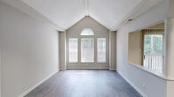 Located at 1823 Club Pkwy in Norcross, GA, this one-bedroom, one-bathroom home offers a well-designed single-floor layout that makes efficient use of every square foot. The living room is the architectural centerpiece of the space, boasting dramatic vaulted ceilings that rise to a peak and a distinctive window grouping — three tall windows topped by a graceful arched transom — that floods the room with natural light and views of surrounding greenery. Durable hardwood-style flooring runs throughout the living area, adding warmth and continuity. The kitchen is thoughtfully updated with crisp white shaker cabinetry, white subway tile backsplash, light quartz-style countertops, and stainless steel appliances including a gas range and full-size refrigerator. The bedroom features plush carpeting, a window for natural light, and access to a dedicated walk-in closet outfitted with wire shelving and hanging rods for ample storage. The full bathroom is clean and functional, featuring a white vanity with a large mirror, updated light fixture, and a full tub-shower combination with wood-look flooring. A hallway connects all rooms cohesively, completing this practical and inviting home in the Norcross community.