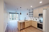 Located at 945 Mid City Drive in Huntsville, AL, this modern one-bedroom, one-bathroom unit offers a well-designed open-concept layout that seamlessly connects the kitchen, dining, and living areas. The kitchen is a standout feature, showcasing light wood cabinetry, a peninsula with a built-in sink and stainless steel dishwasher, a stainless steel range and refrigerator, a tile backsplash with a geometric pattern, open industrial-style shelving, and stylish pendant lighting. Recessed lighting and wood-style flooring run throughout the main living area, adding warmth and continuity to the space. Large floor-to-ceiling windows in the living area and bedroom flood the unit with natural light and frame views of the surrounding urban streetscape. The bedroom is a comfortable size, equipped with a ceiling fan, wood-style flooring, and access to a dedicated walk-in closet with built-in shelving and a hanging rod. The bathroom features a clean, minimalist design with a soaking tub and shower combo, tile surround, and a wood-toned vanity with a stone countertop. Overall, the unit offers a cohesive modern aesthetic with quality finishes throughout.