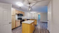 This single-story, 3-bedroom, 2-bathroom home offers a thoughtfully designed layout that maximizes functionality and comfort. The open-concept kitchen, dining, and living area serves as the heart of the home, featuring warm light maple cabinetry, granite-look countertops, a classic white subway tile backsplash, and stainless steel appliances including a range, microwave, and refrigerator. A central kitchen island provides additional prep space and casual seating. Stylish geometric pendant lights add a modern touch to the space, while durable wood-style flooring flows throughout the main living areas. The bedrooms offer a quieter retreat, with plush carpeting and neutral wall tones that create a calm, restful atmosphere. The spacious primary bedroom includes a walk-in closet outfitted with wire shelving for ample storage. The two bathrooms are finished with tile flooring and granite-topped vanities with maple cabinetry; one features a tub-shower combo, while the other offers a glass-enclosed walk-in shower. Additional highlights include crown molding in select areas, a dedicated laundry space, and two closets throughout the home, rounding out a practical and well-organized floor plan.