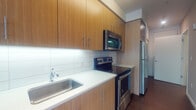 Located at 407 NE Mason St in Portland's vibrant NE neighborhood, this contemporary second-floor unit offers a thoughtfully designed single-level layout with modern finishes throughout. Rich dark hardwood flooring flows seamlessly across the living, sleeping, and kitchen areas, providing a warm and cohesive aesthetic.

The galley-style kitchen is efficiently organized with warm wood-grain cabinetry extending floor to ceiling, bright white quartz countertops, and a clean subway tile backsplash. A full suite of stainless steel appliances includes an electric range, over-the-range microwave, refrigerator, and dishwasher, making this kitchen as functional as it is stylish.

The open living area is bathed in natural light through a large sliding glass door that frames tree-lined outdoor views, lending the space an airy, welcoming feel. A sliding interior door connects the living area to the bedroom, which offers a clean, neutral palette and access to a well-sized closet with built-in shelving.

The bathroom features a wood-grain vanity with a white countertop, a full tub and shower combination, and a crisp, minimalist design. A practical stacked in-unit washer and dryer is conveniently located within the bathroom area, adding everyday functionality to this well-appointed home.
