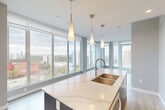Located in Edmonton's vibrant Oliver neighbourhood, this contemporary 2-bedroom, 2-bathroom unit offers a thoughtfully designed open-concept layout with high-end finishes throughout. The living room is anchored by expansive floor-to-ceiling windows that flood the space with natural light and frame sweeping views of the Edmonton skyline and surrounding treetops, creating a bright and airy atmosphere.

The kitchen is a standout feature, showcasing a large island with a striking marble-effect quartz countertop, an undermount double sink, and elegant pendant lighting. Two-tone cabinetry — crisp white uppers paired with rich dark wood lowers — complements the full suite of stainless steel appliances and a classic subway tile backsplash. Light hardwood flooring runs seamlessly throughout the main living areas, enhancing the modern aesthetic.

Both bedrooms are well-proportioned and feature large windows with city views, offering an abundance of natural light. The primary bedroom includes access to a dedicated ensuite bathroom. The two bathrooms are finished with marble-look porcelain tile flooring, dark wood floating vanities with white quartz countertops, and full-surround tiled bathtub enclosures. A welcoming entrance and connecting hallway complete this well-appointed urban residence.