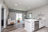 This thoughtfully designed one-bedroom, one-bathroom unit offers a contemporary living experience across a single floor. A welcoming entry hallway with light wood-style flooring leads into the open-concept main living area, where the kitchen and living room flow seamlessly together. The kitchen is outfitted with crisp white shaker cabinetry, light quartz countertops, stainless steel appliances including a range and microwave, and a sink with ample counter space on both sides. An architecturally distinctive feature throughout is the exposed metallic ductwork running overhead, lending the space an industrial-modern character that pairs well with the neutral palette and clean finishes. The living room is bright and inviting, anchored by large sliding glass doors that flood the space with natural light and provide outdoor views. The bedroom offers a cozy retreat with plush carpeting, a generous window with abundant natural light, and a ceiling fan. It connects directly to a spacious walk-in closet with wire shelving on multiple walls. The full bathroom features a tub-shower combination, white vanity cabinetry, and wood-style flooring. A dedicated laundry room with a full-size washer and dryer adds everyday convenience, completing this well-appointed and efficiently organized living space.