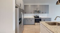 Located at 5306 Acadia Heights Dr in Charlotte, NC, this well-appointed one-bedroom, one-bathroom residence offers a thoughtfully designed single-floor layout with a clean, contemporary aesthetic. The open-concept living and kitchen area is bathed in natural light from large windows with blinds and a glass-paneled entry door, creating a bright and airy atmosphere. Light hardwood-style flooring flows seamlessly throughout the main living spaces, complemented by crisp white walls and clean trim work.

The kitchen is a standout feature, showcasing sleek gray cabinetry with matte black hardware, granite countertops, a white subway tile backsplash, and a full suite of stainless steel appliances including a refrigerator with ice maker, electric range with over-the-range microwave, and a dishwasher. A central island with a undermount sink and stylish pendant lighting adds both functionality and visual appeal.

The bedroom is a comfortable retreat, finished with plush neutral carpeting, a ceiling fan, and windows that invite natural light. The bathroom continues the home's refined design language with gray cabinetry, granite countertops, an undermount sink, framed mirror, and wood-look flooring. A dedicated closet with built-in shelving provides ample storage. Recessed lighting and a cohesive neutral palette tie the entire space together.