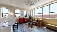 This single-floor urban residence offers a well-designed open-concept layout that seamlessly connects its main living areas. The spacious living room is a standout feature, boasting expansive floor-to-ceiling windows that frame sweeping city views and flood the interior with natural light. A ceiling fan adds comfort, while wood-look flooring and a boldly accented teal wall contribute to the space's modern yet eclectic character. Exposed ductwork lends an industrial touch to the overall aesthetic.

The kitchen is thoughtfully appointed with dark espresso cabinetry, granite countertops, and black appliances. A large central island with bar seating provides additional workspace and casual dining, while pendant lighting overhead adds a refined finishing touch. The kitchen's open sightlines integrate effortlessly with the dining and living areas.

Two bedrooms offer comfortable retreats, each featuring plush carpeting, generous windows with city outlooks, and soft neutral tones. The two bathrooms are finished with dark vanity cabinetry, light countertops, tile flooring, and well-lit mirrors, maintaining a consistent and cohesive design language throughout the residence. Together, these spaces create a functional, light-filled urban home with a distinctly contemporary character.